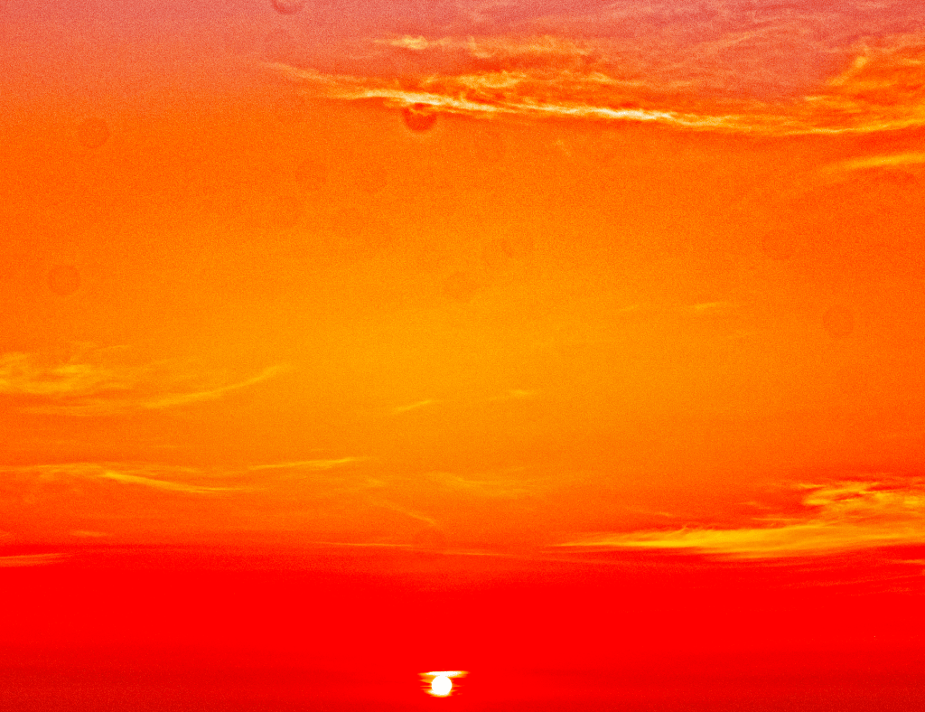 Fiery orange sunset with a glowing sun near the horizon over a dark, calm sea/landscape.